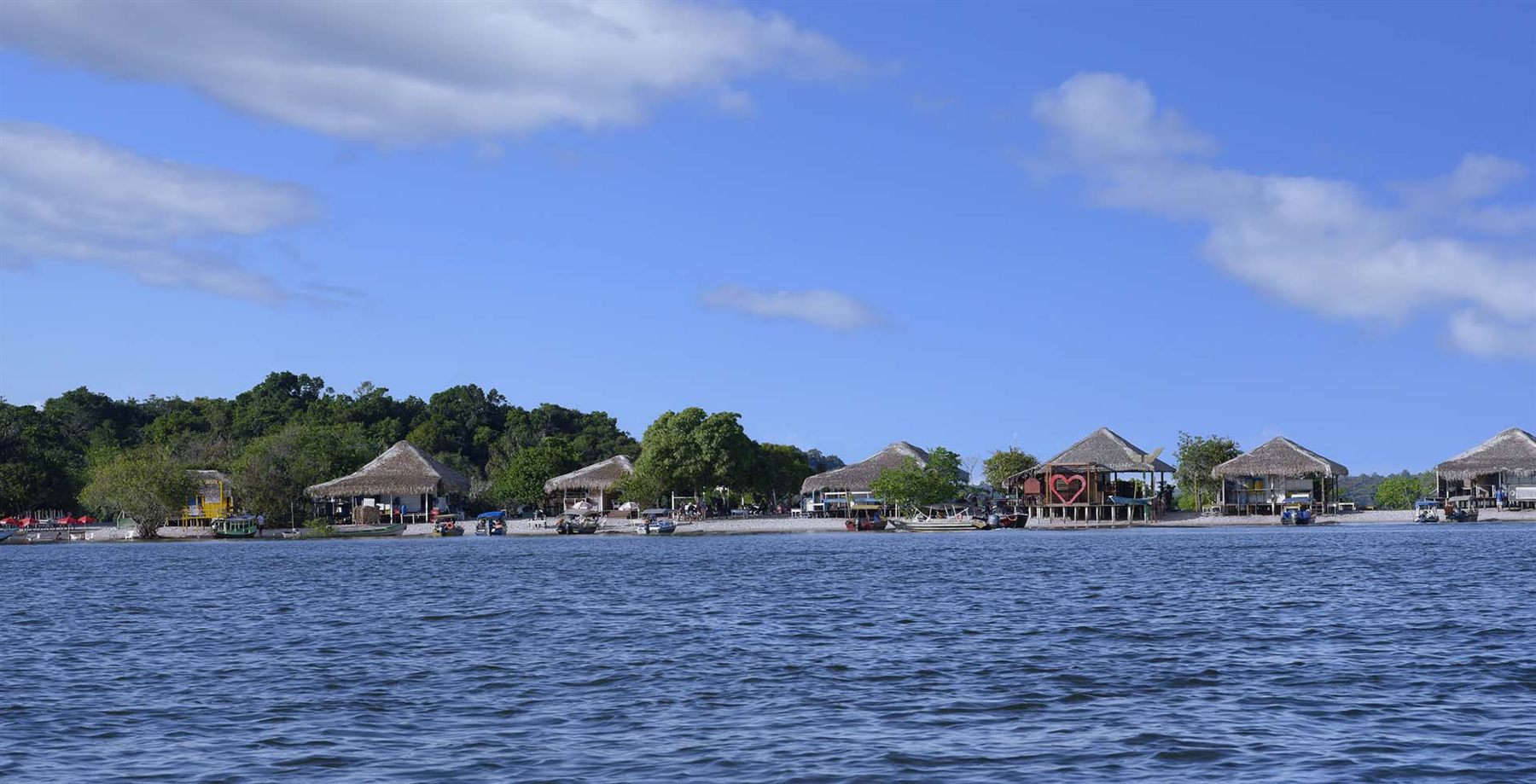 Thatched riverside huts and small boats on a sandy Amazon shore